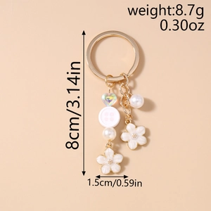 Detailed close-up of golden floral keychain with white enamel petals and pearl charms