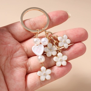 Detail of gold keychain with white enamel flowers, faux pearls and a heart pendant