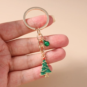 Porte-clés sapin de Noël avec clochette verte et anneau doré tenu sur fond rose pastel