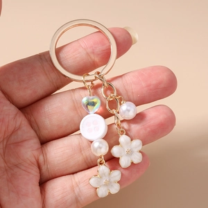 Detail of floral keychain with colorful heart, pearls, and white flower charms on a golden ring