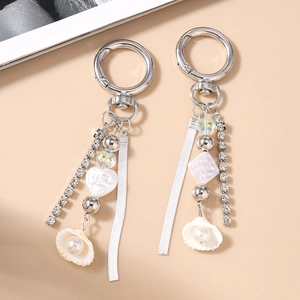 Silver beaded keychain with pearl shell heart charms and rhinestone tassel on beige background