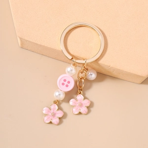 Detailed view of gold keychain with pink cherry blossoms, faux pearls, and button charms