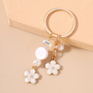 Detail of floral keychain with gold ring, white enamel flowers, and iridescent heart charm