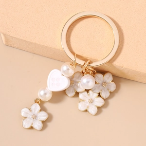Close-up of golden keychain with white enamel cherry blossoms and faux pearls