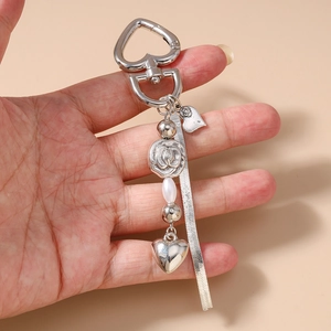 Detail view of silver heart keychain with rose bead, faux pearl, and snake chain on hand