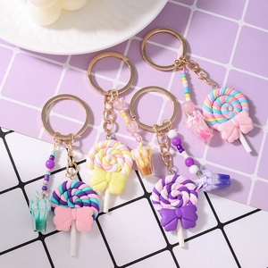 Colorful swirl lollipop keychains with bows and mini drink charms on a grid background