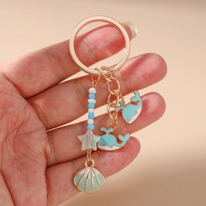 Detail of a golden ocean-themed keychain with blue whale and green shell enamel charms