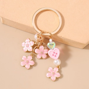 Detailed view of a gold keychain with pink enamel cherry blossoms and white pearls