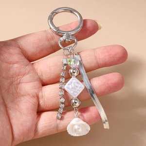 Detail of beaded keychain with shell pearl charm and rhinestone tassel held in hand