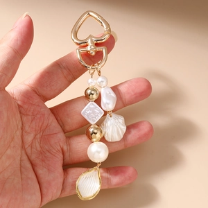 Détail du porte-clés en perles avec fermoir cœur et pendentif coquillage à la main