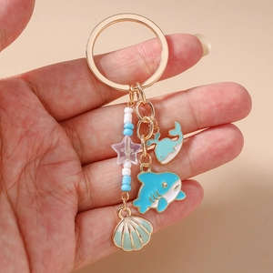 Detail of ocean-themed keychain with blue whale, shark, and shell charms on gold ring