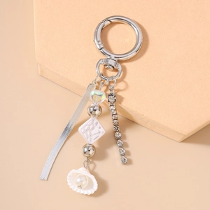 Detailed view of silver snake chain keychain with pearls, shell, and rhinestone tassel