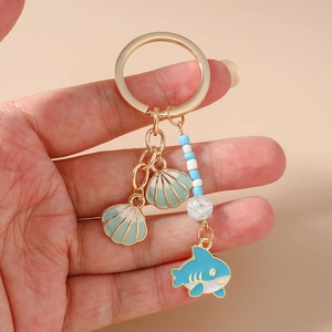 Detail of hand-held nautical keychain with blue shark charm and green enamel shell pendants