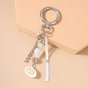 Detail of silver keychain featuring rhinestone tassel, pearly heart, and seashell charm