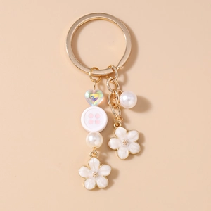 Detail of floral keychain featuring white enamel flowers, pearls and pink button charm