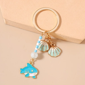 Detail of shark and shell charms on golden keychain with blue beads over beige stone