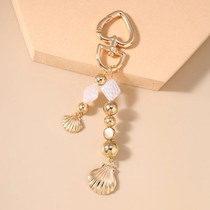 Vue détaillée de pendentifs coquillages dorés et perles sur le porte-clés cœur