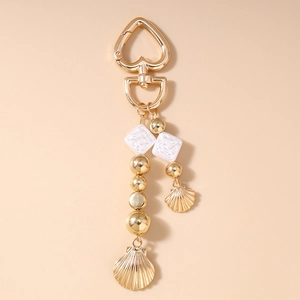 Détail de breloques coquillage et fermoir cœur sur un porte-clés doré avec perles
