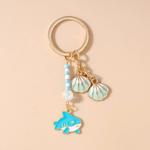 Detail of shark enamel pendant and mint sea shell charms on a gold tone keychain