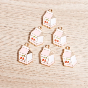 Flat lay of pink milk carton charms with cherry design and gold alloy hanging loops