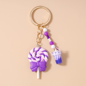 Close-up of a purple lollipop keychain with drink charm and beaded tassel on a gold ring