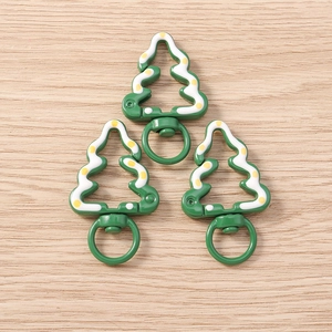 Close-up of green Christmas tree keychains with white dots on light wood background