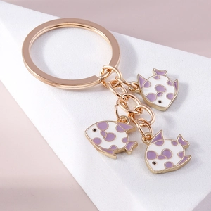 Detail view of goldfish charms on a gold keychain with white and purple enamel pattern
