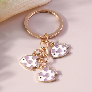 Detail of goldfish enamel keychain with purple dots and gold hardware on a shell background