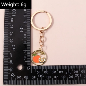 Détail du porte-clés orange doré avec mesure de la taille sur fond rose clair