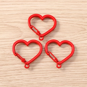 Close-up of bright red heart-shaped spring snap hooks on a natural wooden surface