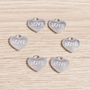Macro detail of six silver plated heart charms with LOVE engraving on a wood background