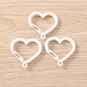 Three white heart-shaped spring snap hooks on light wood background for DIY accessories