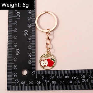 Détail porte-clés pomme or rose avec gravure et règle de mesure de 10cm sur fond rose