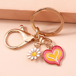Golden heart keychain with white daisy and oil-painted pink heart pendant on warm background