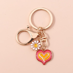 Detail of heart enamel charm and daisy flower pendant on golden keychain hook