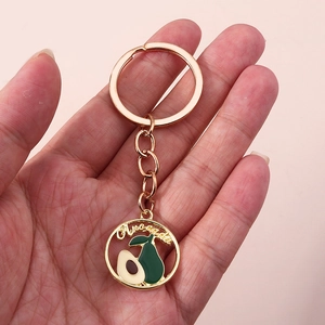 Gros plan sur le porte-clés doré avec charme rond évidé et pendentif avocat en émail