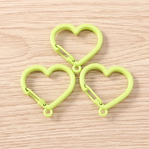 Three mint green matte heart carabiners with spring clips on light wood surface
