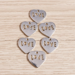 Detailed view of silver heart-shaped LOVE charms on wood for DIY jewelry making