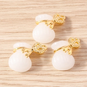 Three creamy resin lucky bag pendants with golden bow accents on a light wood background