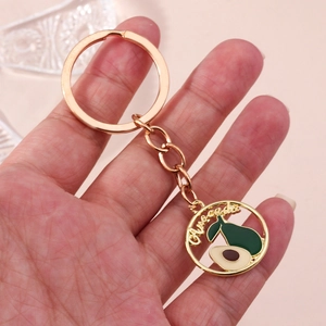 Détail d'un porte-clés avocat en métal doré avec pendentif rond évidé tenu à la main