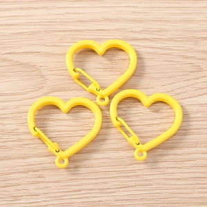 Macro view of three yellow heart-shaped metal carabiner hooks on a wood background
