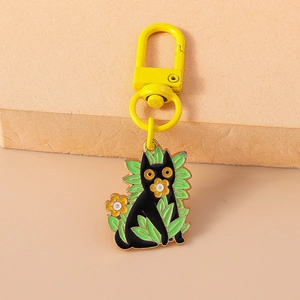 Détail d'un porte-clés émaillé avec chat noir, fleurs et attaches métalliques jaunes