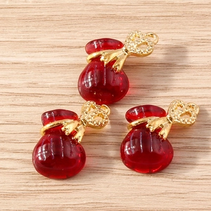 Three red resin fortune bag charms with gold metal caps on a wooden background for jewelry DIY