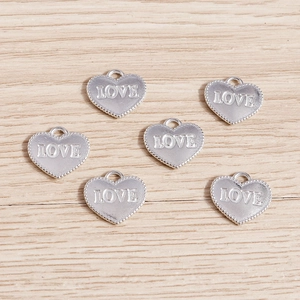 Macro shot of silver plated heart charms with LOVE engraving and beaded edge details