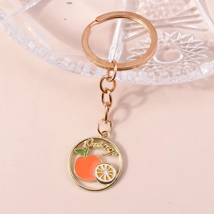 Détail d'un porte-clés doré avec charm orange en émail et texte Orange sur fond rose pastel