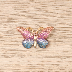 Detailed macro view of colorful enamel butterfly charms with gold metal frames for DIY crafts