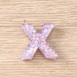 Detailed macro of a purple sequin star resin letter X pendant with golden ring