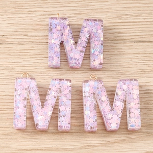 Close-up of purple resin letter M pendants with sparkling sequins and gold metal rings