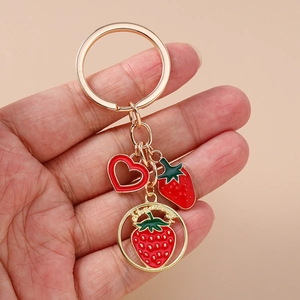 Fashionable red strawberry keychain with heart charm and golden ring on a clean background