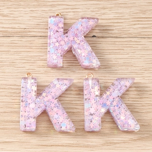 Close-up of three pink resin letter K pendants with colorful star sequins and gold loops